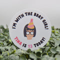 A round white sticker with a cartoon character and the text 'I'M WITH THE BDAY GIRL! TINA IS 13 TODAY!' placed on green foliage against a light gray background.