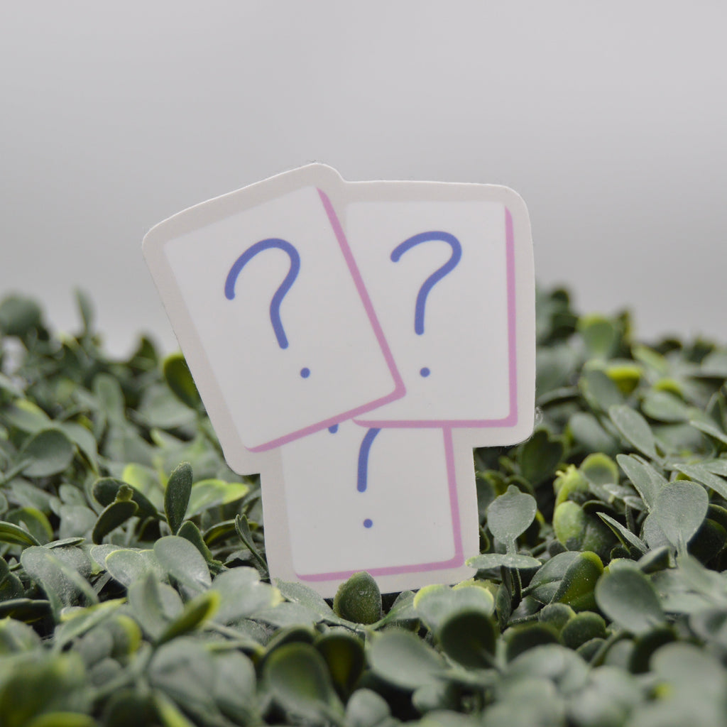 Three small white cards with blue question marks and pink borders are placed among green leaves against a soft gray background.