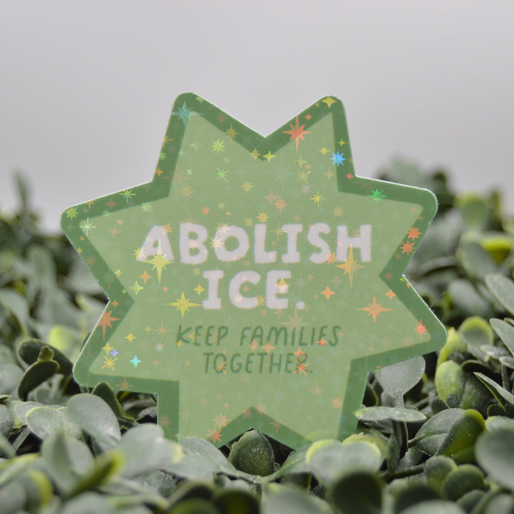 Green Star Shaped Sticker with white text reading "abolish ice, keep families together" on a blurred leaf background.