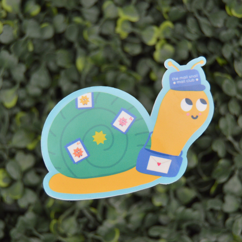A cartoon snail with a yellow body, blue hat, and green shell, placed against a blurred green hedge background.