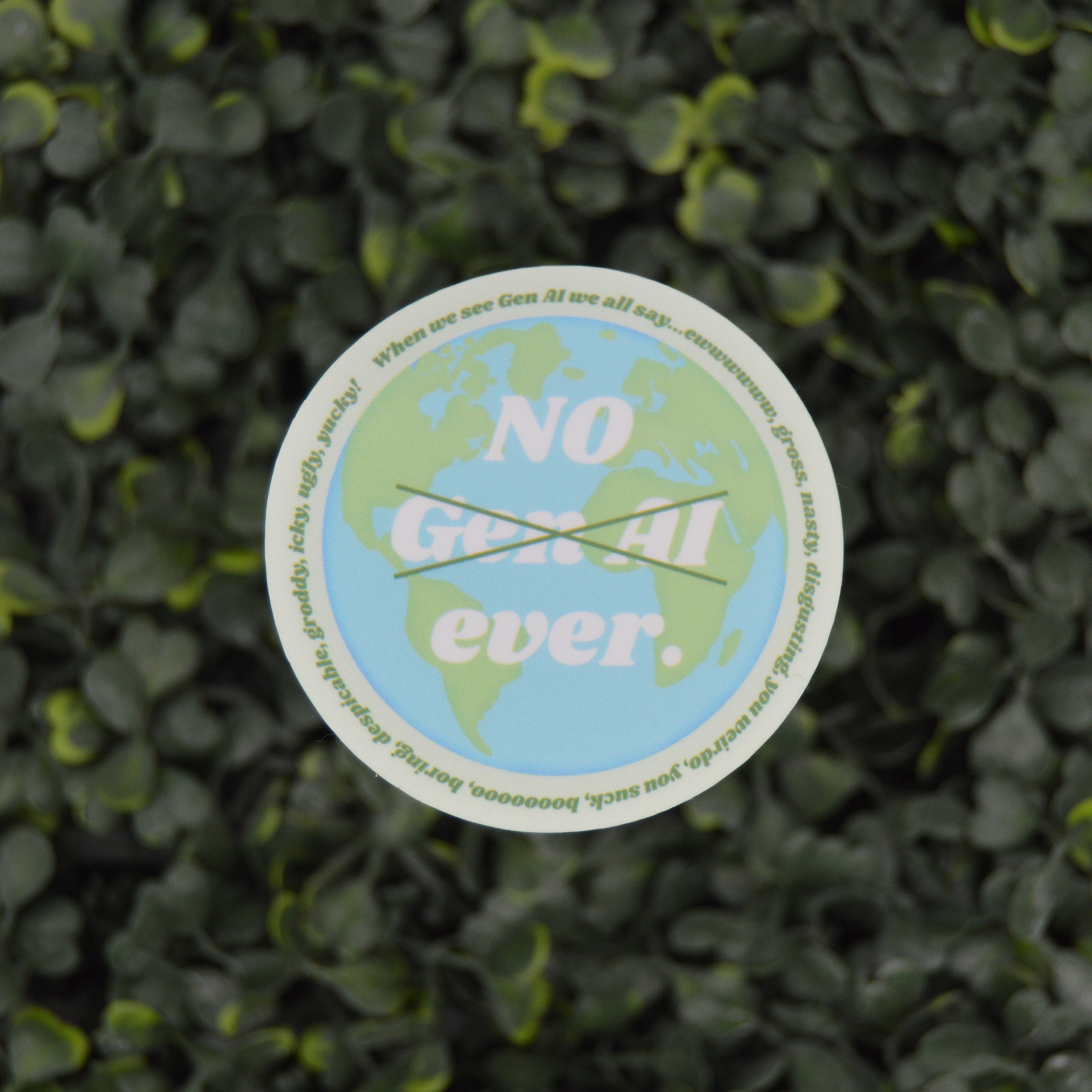 A circular sticker with a green and blue globe design and the text 'NO Gen AI ever.' crossed out placed on a background of dense green leaves.