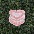 A die-cut sticker featuring a pink and white illustrated cake with the text 'I have depression!' in pink, placed against a background of dense green ivy.