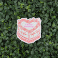 A die-cut sticker featuring a pink and white illustration of a cake with the text 'I have anxiety!' in pink, placed against a background of green foliage.