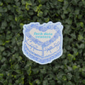 A die-cut sticker featuring a blue and white illustrated cake with the text 'fuck data centers' in light blue, placed against a background of green variegated foliage.