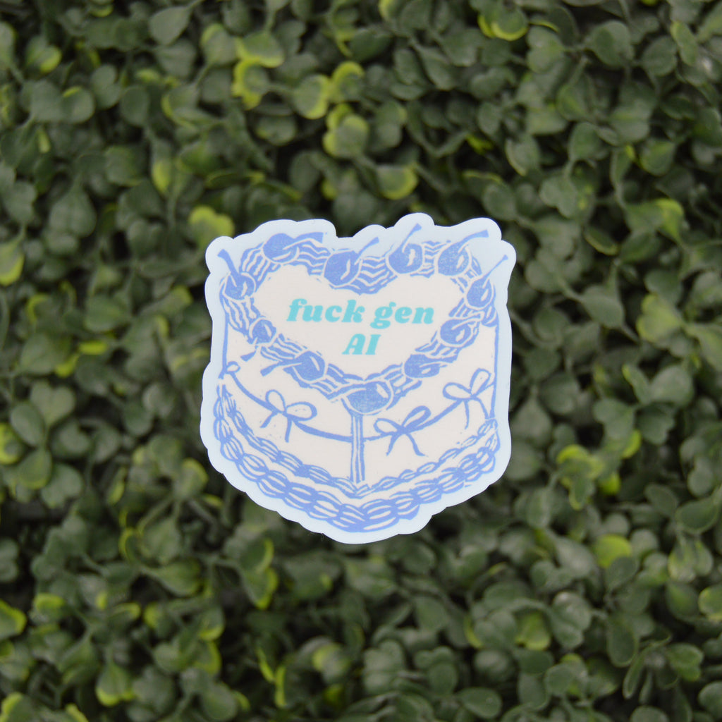 A die-cut sticker featuring a blue and white illustrated cake with the text 'fuck gen AI' in light blue, placed against a background of green ivy leaves.
