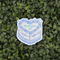 A die-cut sticker featuring a blue and white illustrated cake with the text 'fuck gen AI' in light blue, placed against a background of green ivy leaves.