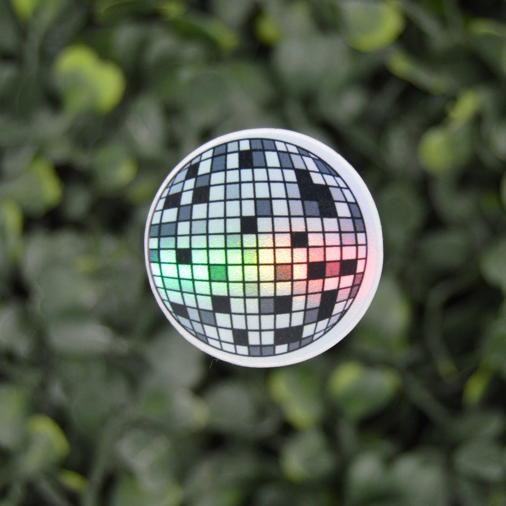 A round sticker featuring a black and white disco ball design with a green, yellow, and red light effect, shown against a blurred green leaf background.