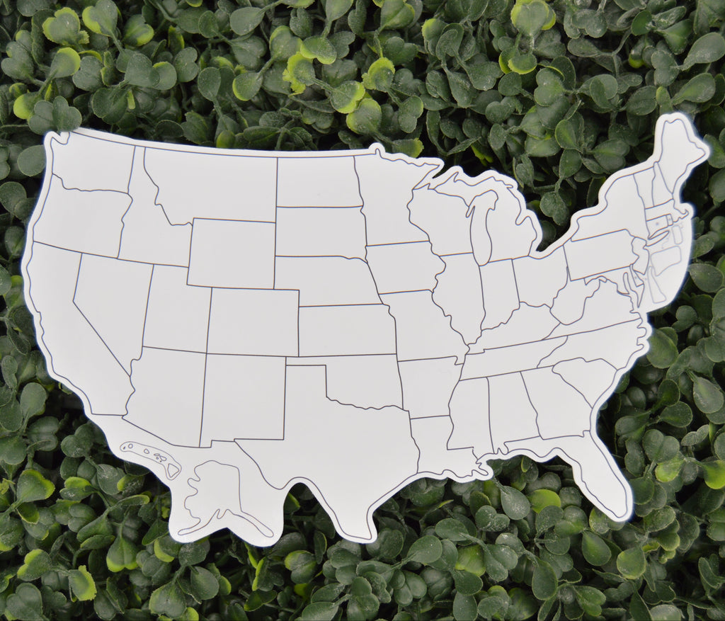 A white die-cut map of the United States with black state outlines, photographed from above against a dense green leafy hedge background.