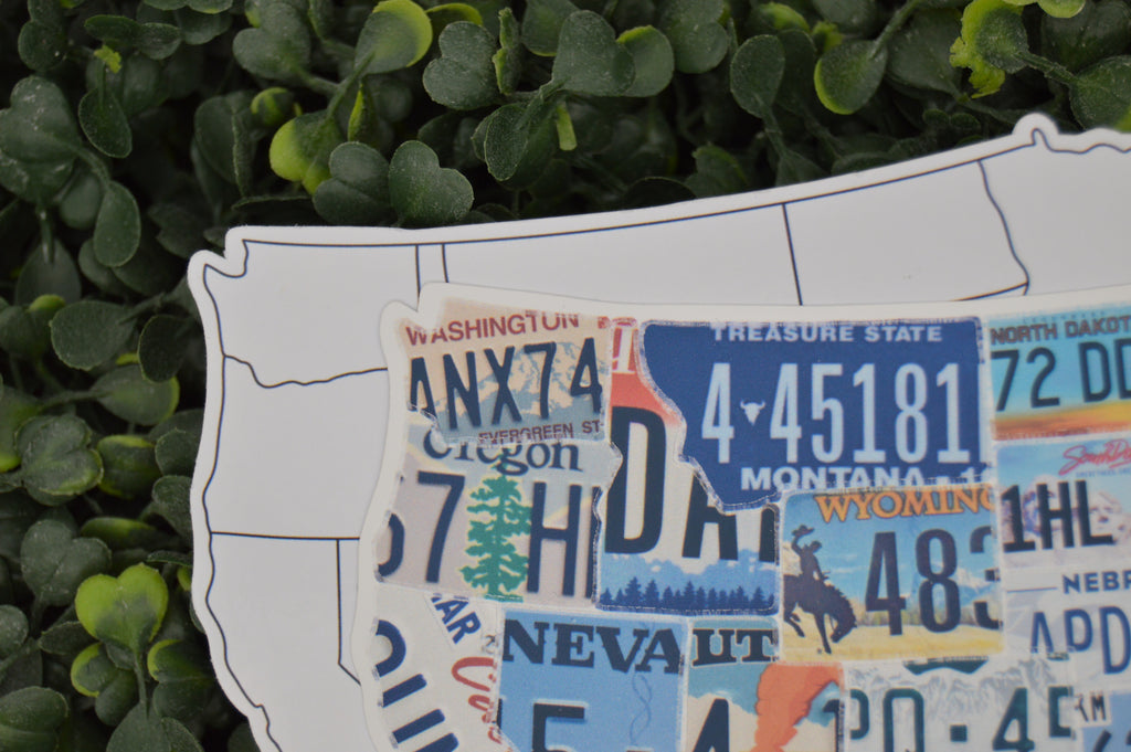A USA-shaped wall art piece made from colorful vintage license plates, displayed against a background of green foliage.