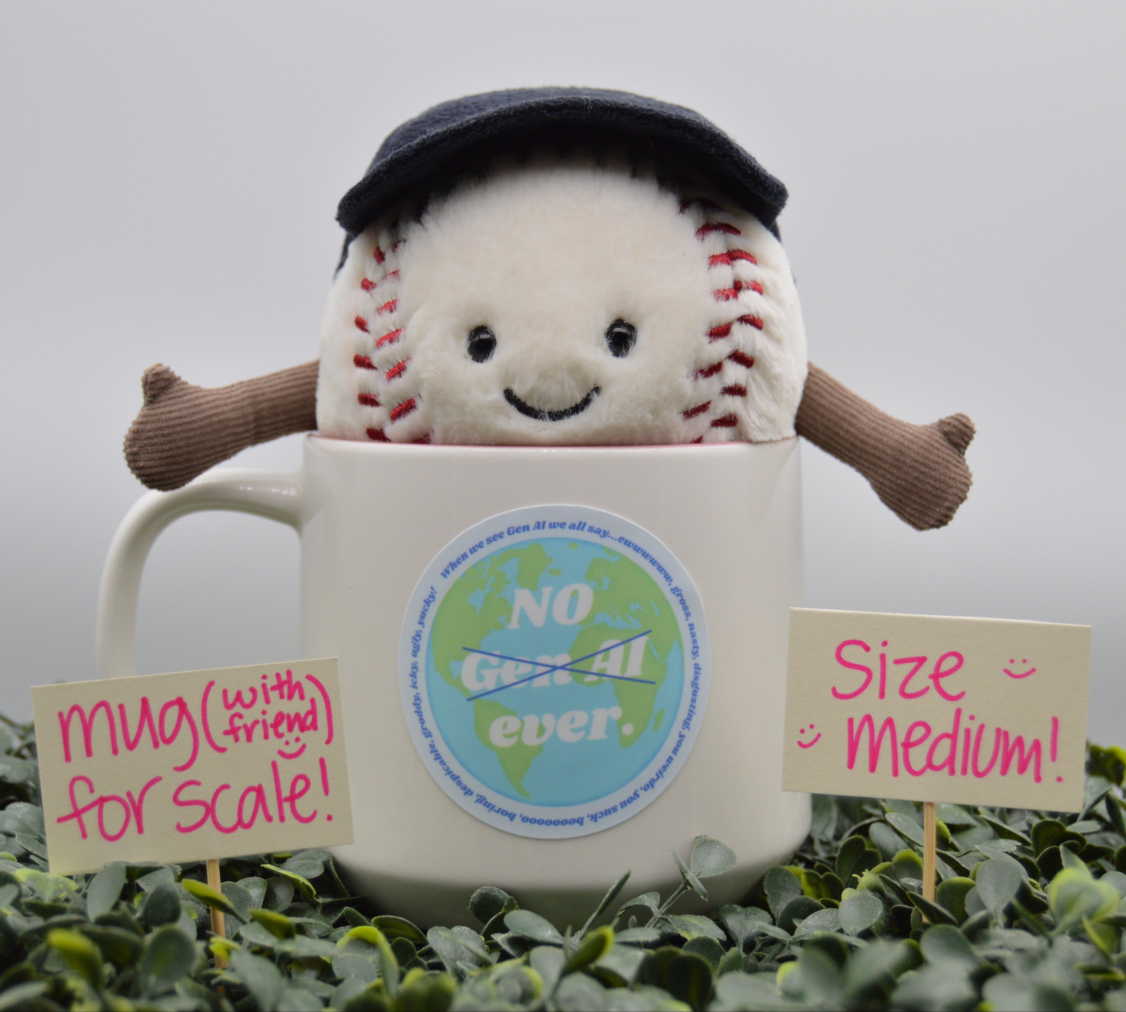 A plush baseball toy wearing a dark navy cap and brown arms, sitting inside a white ceramic mug. The mug has a circular 'No Gen AI ever sticker.